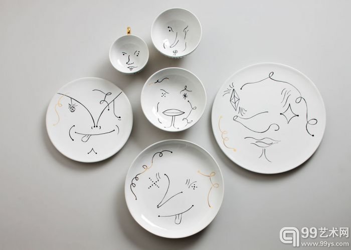 他还有一套瓷器做的餐具，有盘子、杯子和碗，里面画着漫画式的人脸，有点像小丑。在黑色线条的中间穿插一两根金色的线，是提亮和活泼的变调，也与木偶烛台的用色一致。