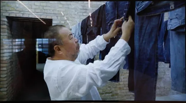“自助洗衣店”展览现场的纪录片截屏，显示艾未未在整理难民衣物。图片来源：王悦