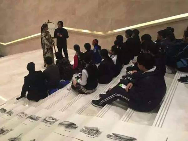 来自青海果洛的藏族学生和市民围坐在楼梯上，一边看画，一边听周培元讲述建筑中的艺术奥秘。