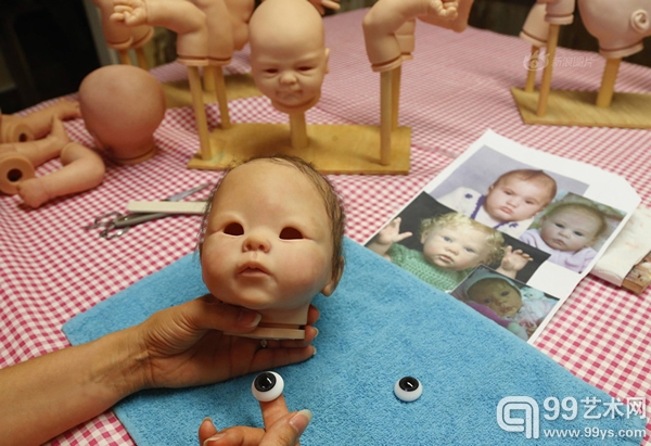 工作室的桌子上摆放有很多玩偶的身体部件，艺术家比阿特丽丝正在给一个重生娃娃安装眼球，她会根据宝宝们的照片做出一个个逼真的“婴儿”。